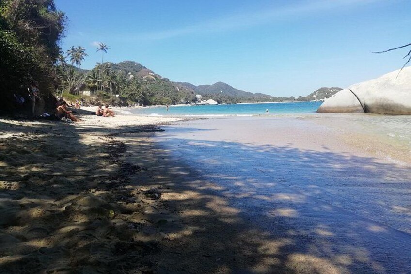 A beach with clear water, a sandy shore, and a large rock formation. 2