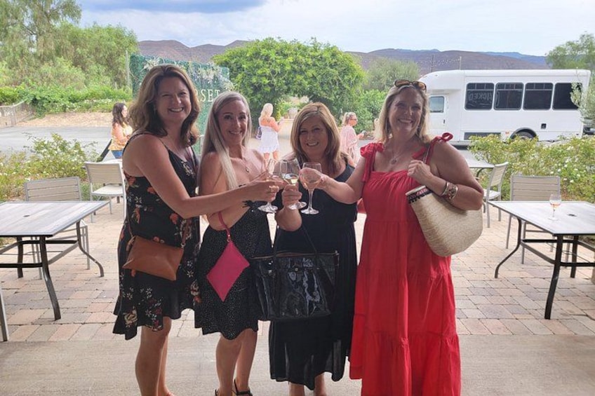 A group of people toasting with wine glasses outdoors, with tables and chairs, and a bus in the background. 2