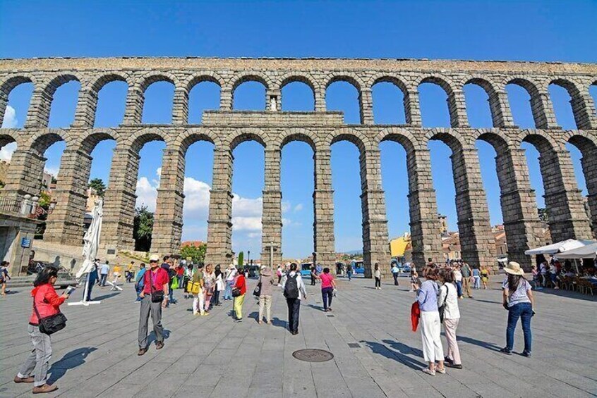 An ancient aqueduct with multiple arches and a crowd of people in a plaza. 3