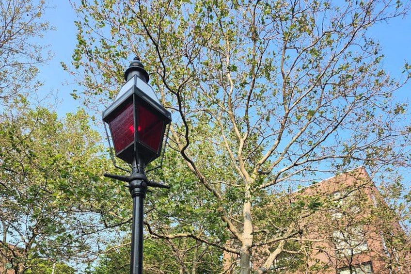 A street lamp with a red light, surrounded by trees and a building in the background. 2