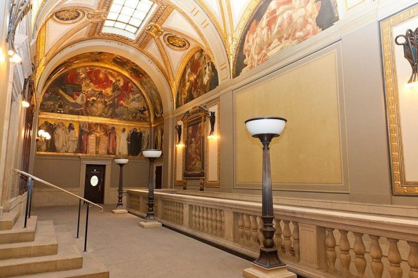 An ornate hallway with a grand staircase, a chandelier, and a large mural on the wall. 3