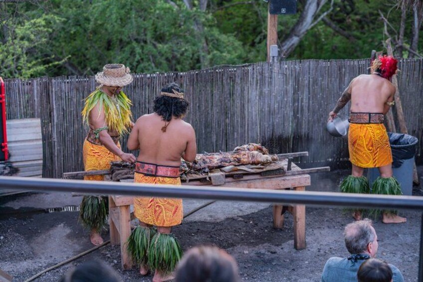 A traditional cooking scene with people in native attire, a wooden structure, and a dirt ground. 2