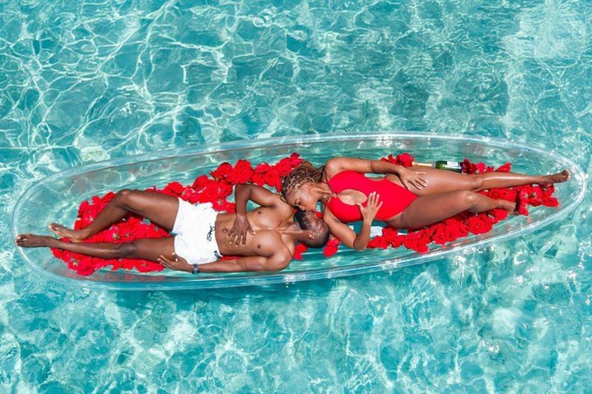 Two people lying on a floating platform in a pool surrounded by red rose petals. 1
