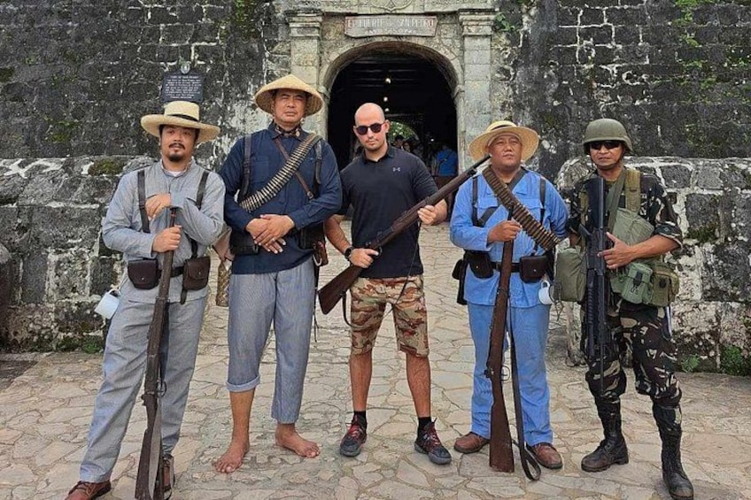 Un grupo de hombres con vestimenta histórica frente a un edificio de piedra con una entrada arqueada. 3