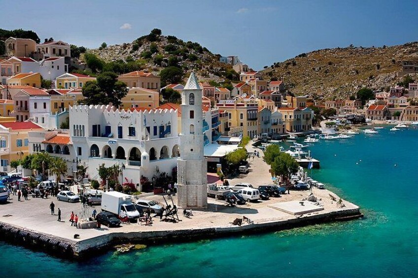 Un pueblo costero con una torre blanca destacada, edificios coloridos y un puerto deportivo. 2