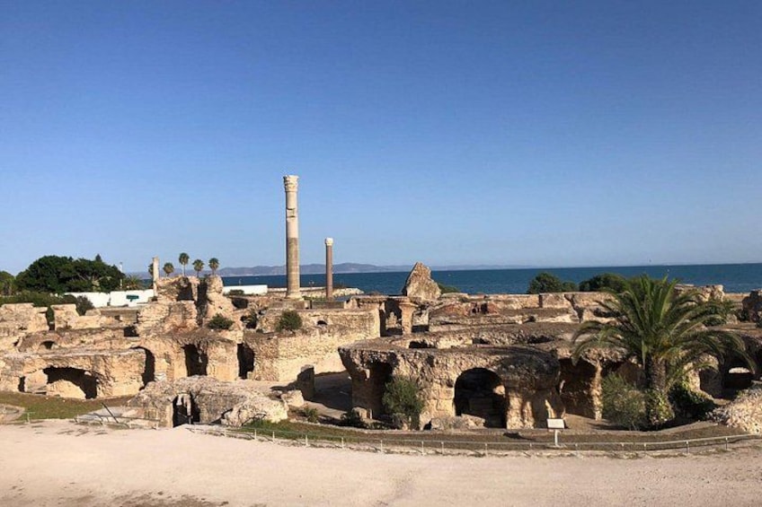 Des ruines antiques avec des colonnes et des arches, un palmier et un ciel dégagé. 3