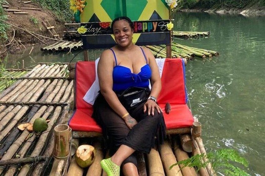 Una persona sentada en una balsa de bambú con un letrero que dice 'happy day', rodeada de agua y follaje. 2