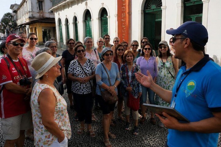 A group of people gathered around a guide in a historical area with white buildings and green doors. 1