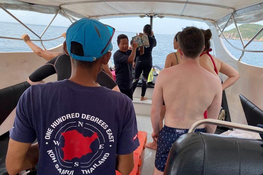 Des personnes se trouvent sur un bateau, certaines portent des chapeaux, et on peut voir une carte imprimée sur un t-shirt. 3