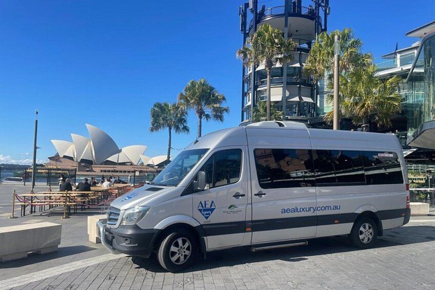 A white van parked near a waterfront with palm trees and a modern building in the background. 2