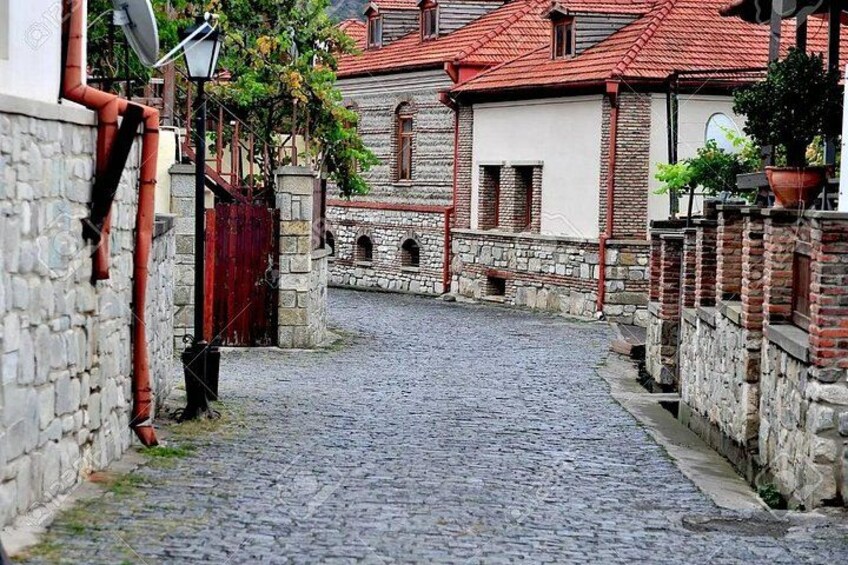 A cobblestone street in a historic town with stone walls, a red gate, and traditional buildings. 2