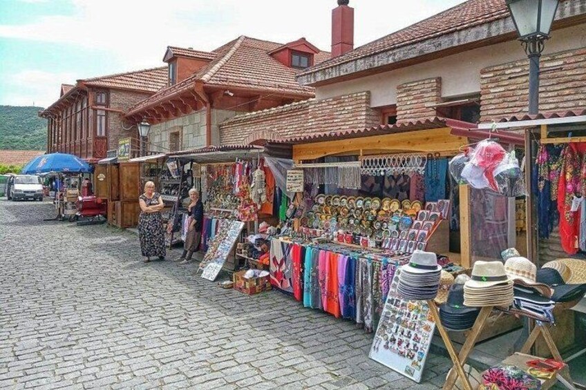 A cobblestone street with a market stall selling hats and textiles. 5