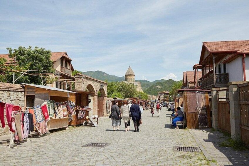 A cobblestone street with people walking, buildings with red-tiled roofs, and a mountain in the background. 3