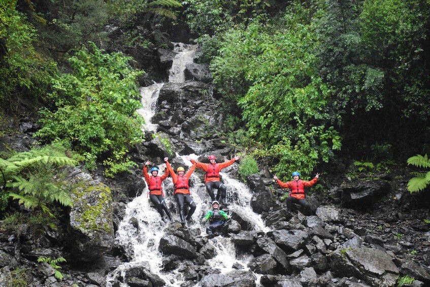 Un grupo de personas con chalecos salvavidas rojos saltando desde una cascada en un área boscosa. 5