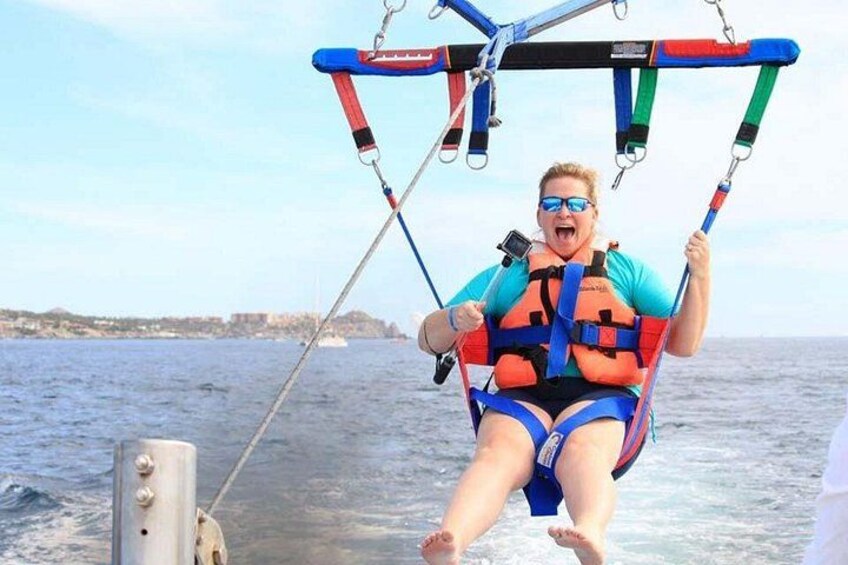 A person on a swing chair attached to a boat, wearing a life jacket, with the sea and a distant shoreline in the background. 4