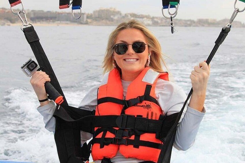 Een persoon op een parasail, met een camera, een redingsvest en vastgrijpend aan het tuig. 3