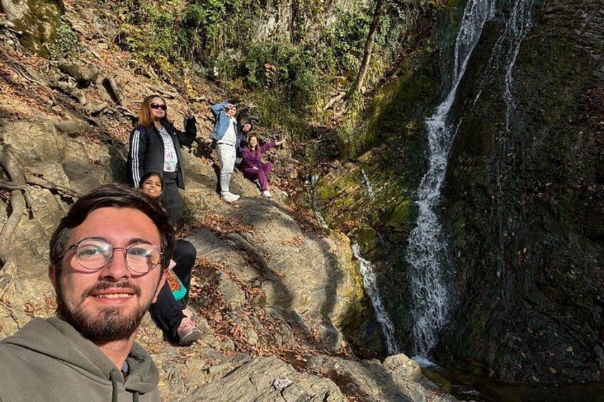 Eine Gruppe von Personen auf einem felsigen Pfad, im Hintergrund ein Wasserfall. 3