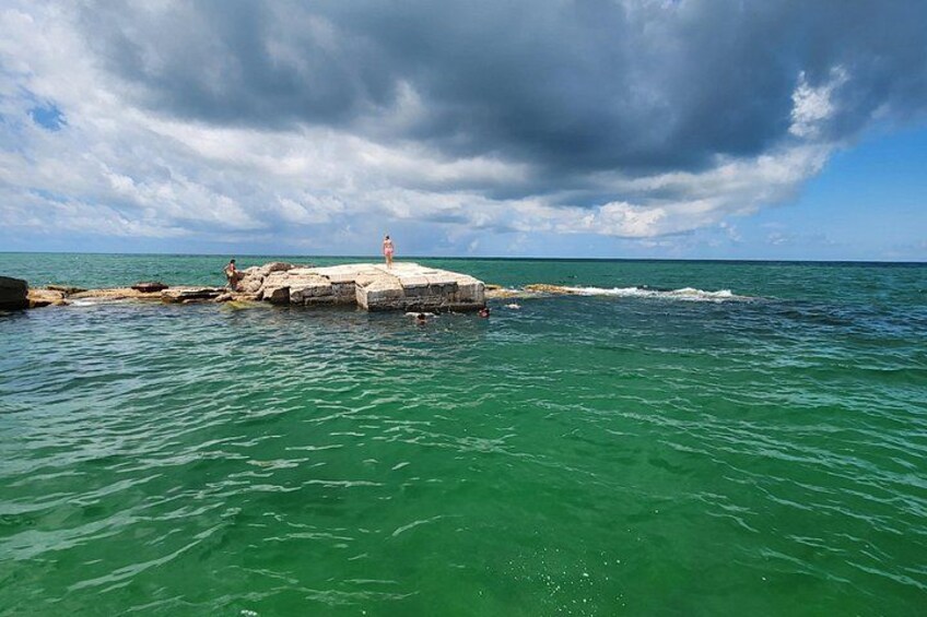 Una scogliera rocciosa nell'oceano con acque turchesi cristalline e un cielo nuvoloso. 3