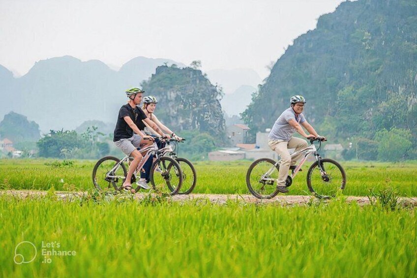 Two people riding bicycles on a rural road with green fields and mountains in the background. 4