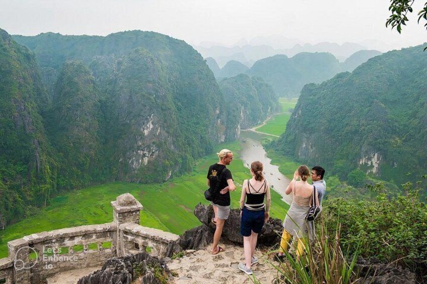 A group of people standing on a stone platform overlooking a river valley with lush greenery and steep cliffs. 5