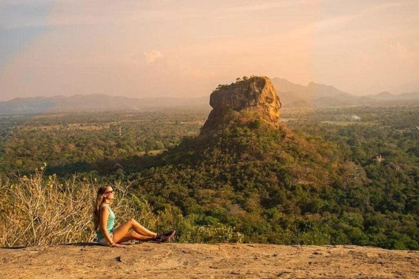 A person sitting on a hill overlooking a landscape with a prominent rock formation. 1
