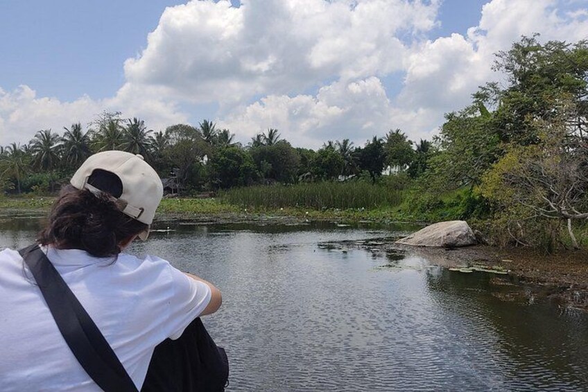 A person taking a photo of a calm river with trees and rocks in the background. 3