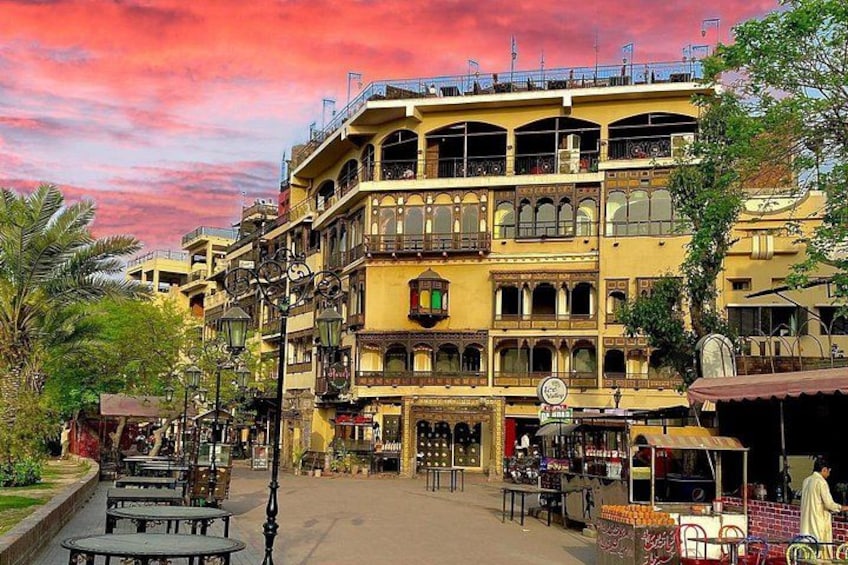 Calle con edificios de varios pisos, mesas al aire libre y un puesto de mercado. 2