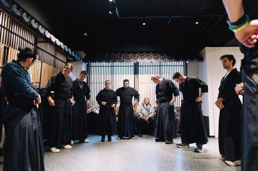 Un groupe de personnes, vêtues de costumes traditionnels, se tient dans une pièce dont l’aménagement intérieur est de style moderne. 2