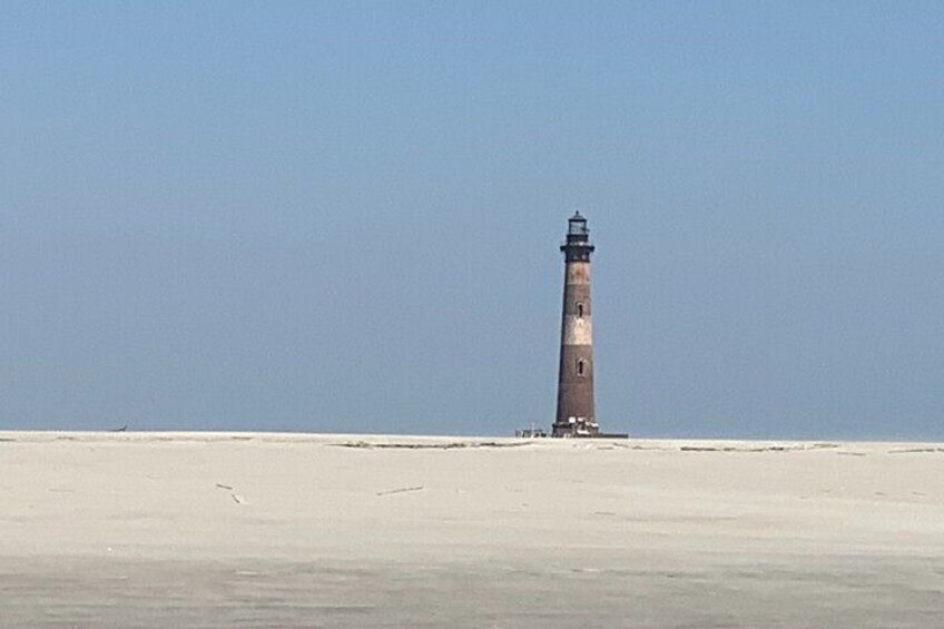 Ein Leuchtturm an einem sandigen Strand bei blauem Himmel. 1
