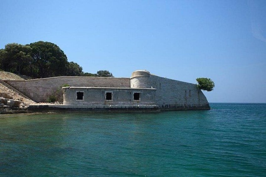 Une fortification côtière dotée d’une tour ronde et d’un bâtiment rectangulaire, entourée d’une mer calme et d’un ciel dégagé. 4
