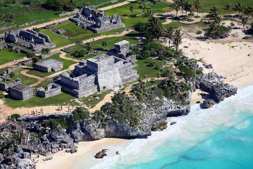 An aerial view of a coastal archaeological site with ancient ruins, a sandy beach, and a clear turquoise sea. 5