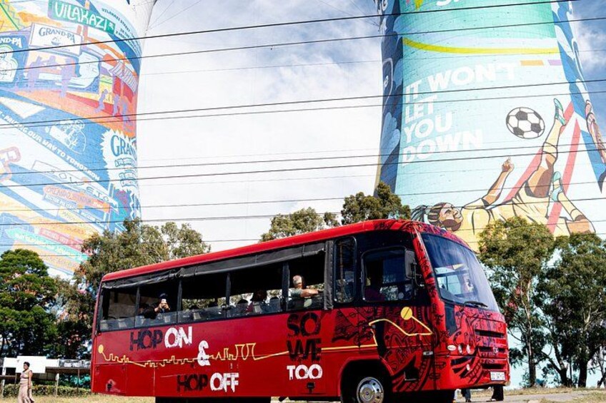 A red bus with graffiti and advertisements, parked in front of a colorful mural. 2
