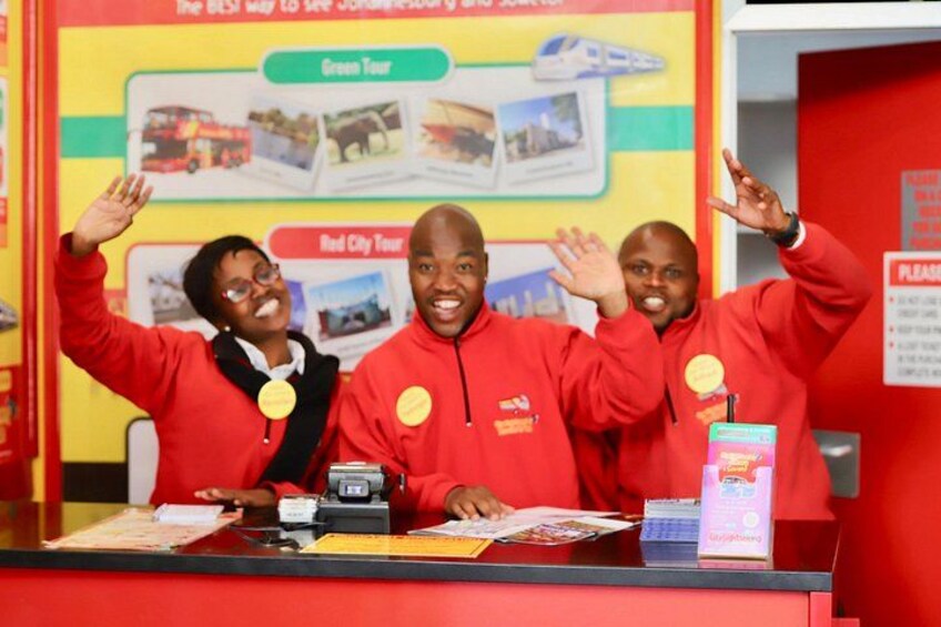 Three people in red jackets with badges, a red counter, and a sign about tours. 4
