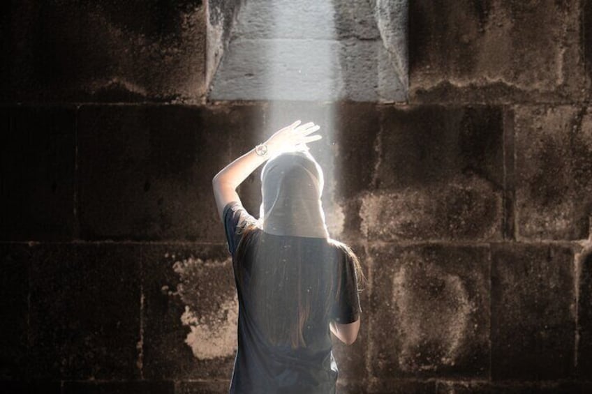 Una persona de pie frente a un muro de ladrillo con una fuente de luz en la parte superior. 3