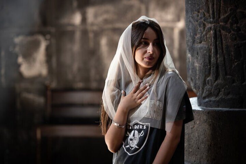 Una persona con camiseta de los Raiders y un velo, de pie frente a un muro de piedra con grabados. 4