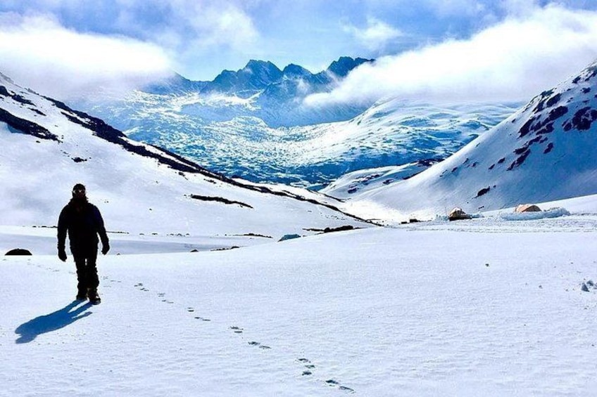 A person walking on a snow-covered path with mountains in the background. 1