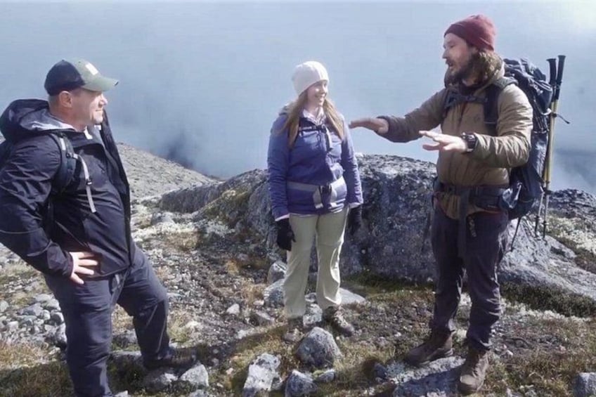 Three people hiking on a rocky mountain trail with a lake in the background. 4
