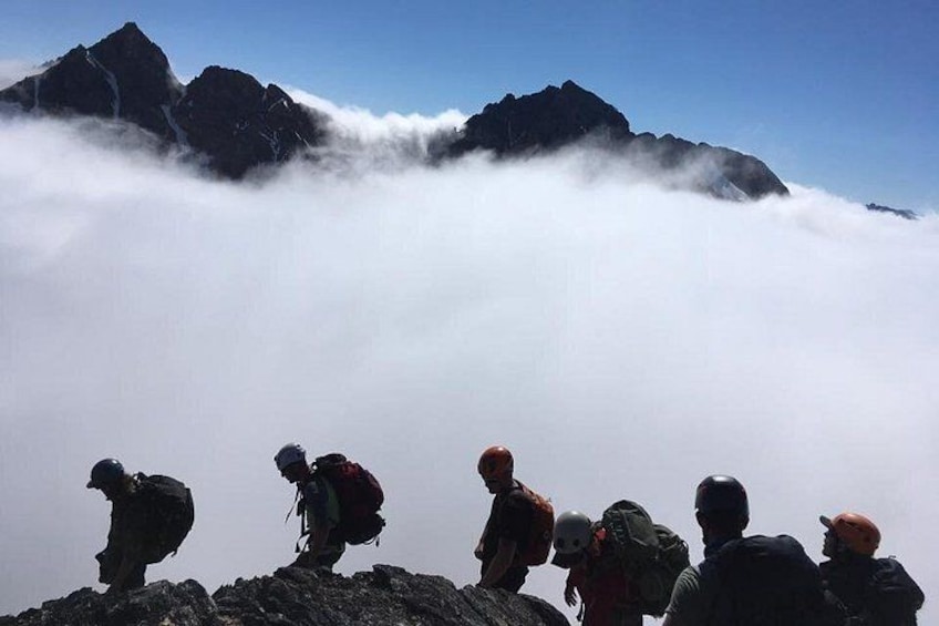 A group of hikers on a mountain peak with clouds below. 5