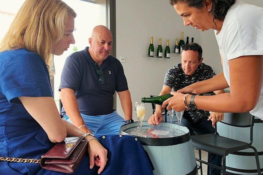 A group of people sitting around a table with a bottle of champagne being opened. 4