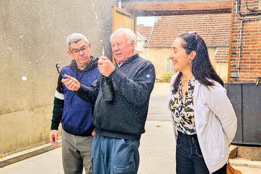 Tres personas de pie al aire libre, una sosteniendo un atomizador, con un edificio de ladrillo y una cerca al fondo. 5