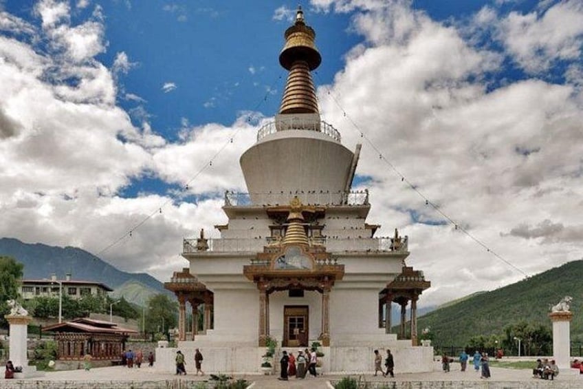 A large white stupa with a golden spire, surrounded by a square courtyard with people walking around. 3