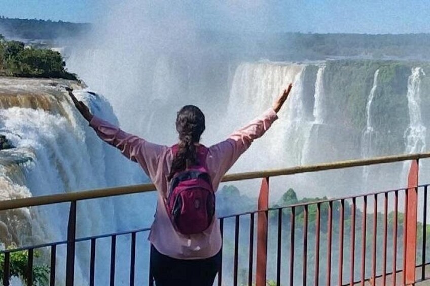 A person with arms outstretched, facing a large waterfall. 3