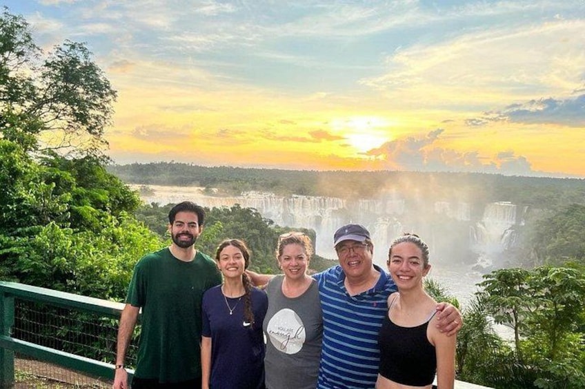 Een groep mensen staat voor een waterval, met een zonsondergang op de achtergrond. 4