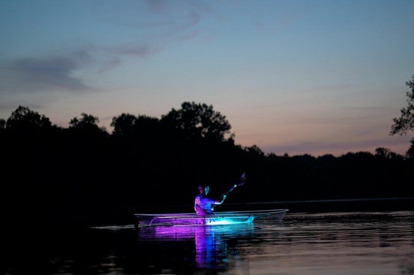 A person fishing at dusk on a calm body of water with trees in the background. 2