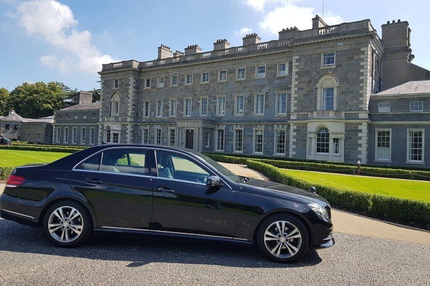 A black sedan parked in front of a large, historic building with a well-manicured lawn and a clear sky. 5