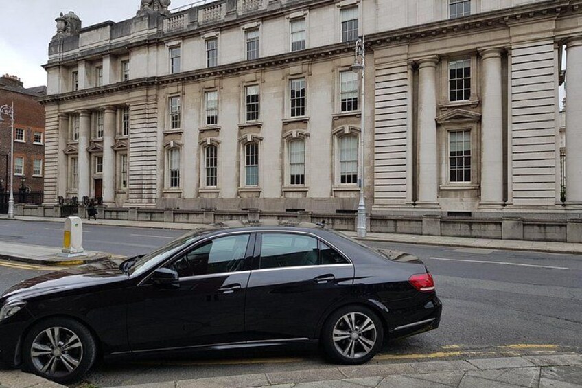 A black car parked on a city street in front of a large, classical building with columns and large windows. 2