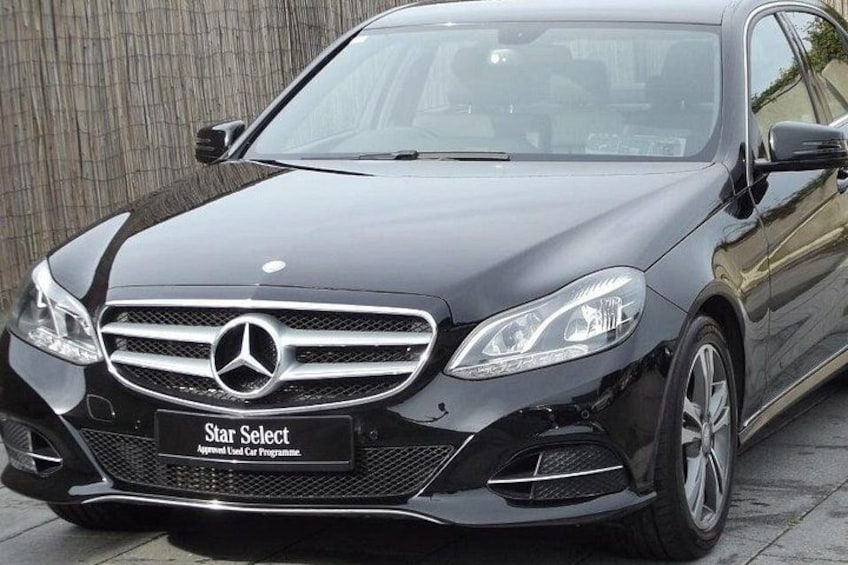 A black Mercedes-Benz car parked on a paved surface with a wooden fence in the background. 1