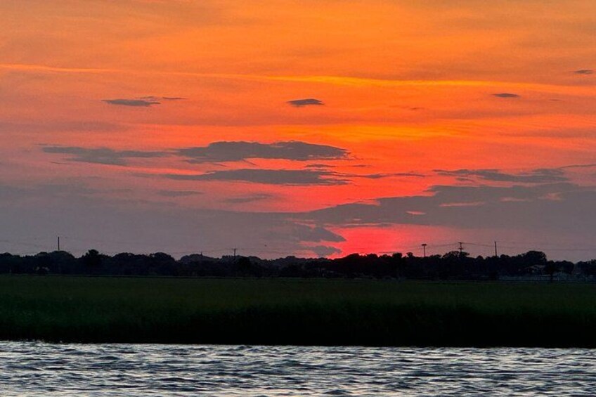 A sunset over a body of water with silhouettes of trees and a distant horizon. 3