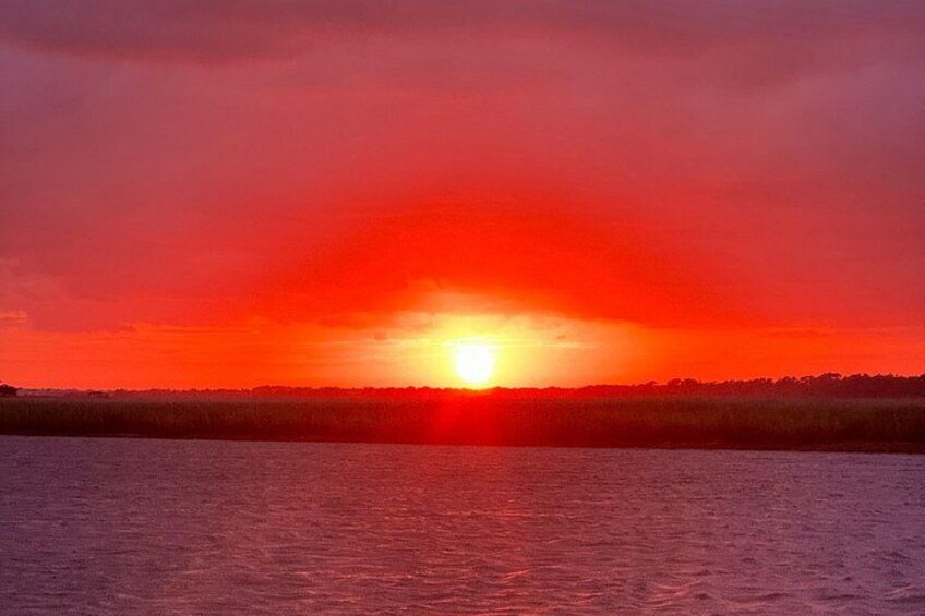 A sunset over a body of water with a silhouette of trees in the distance. 4