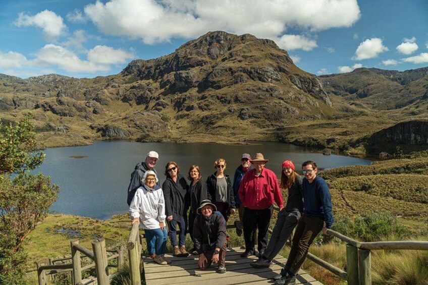 A group of people on a wooden boardwalk with a lake and mountains in the background. 2